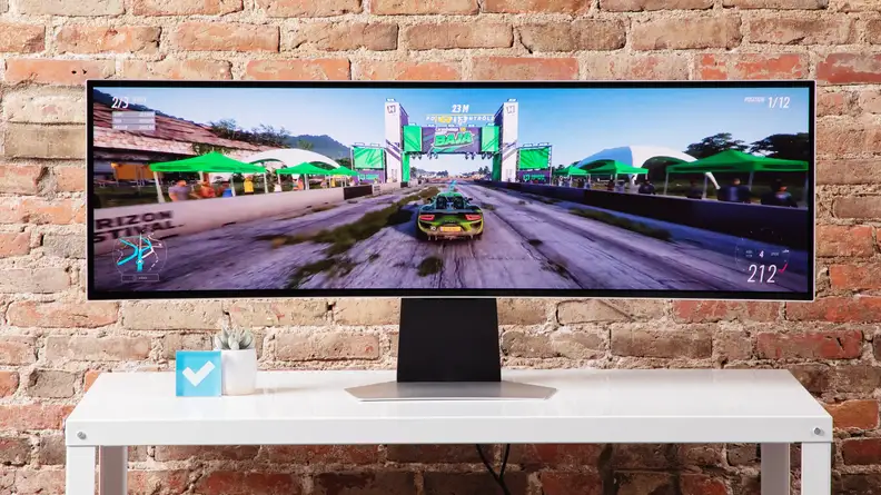 The Samsung Odyssey OLED G9 on a white desk with a brick background.