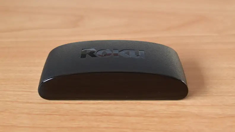 The Roku Express 4K+ sits as a rounded black box atop a light, woodgrain surface.