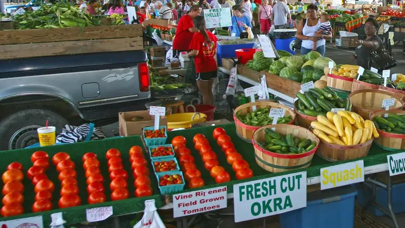 Market stand with tomatoes, squash, and "Fresh Cut Okra" signage