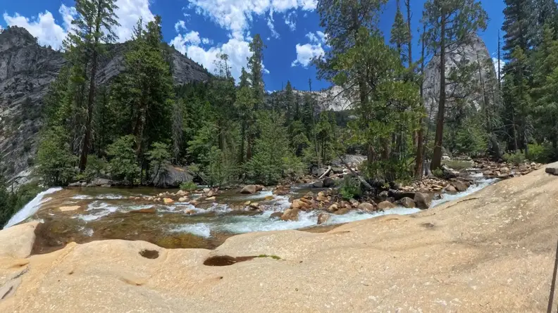 A scenic view of a babbling brook, trees and a mountain on the sunny day.