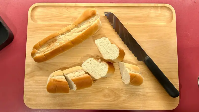 A cutting board with a knife and cut French bread on top.