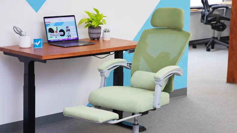 Green Ergonomic Office Chair with footrest extended, positioned in front of desk with laptop computer .
