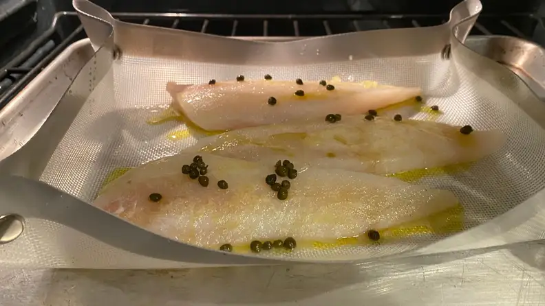 Folded-up baking mat with three pieces of fish baking inside, shot from the oven.
