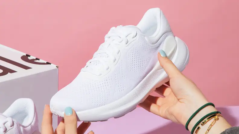Person holding a single, white lululemon BeyondFeel shoe next to cardboard box.