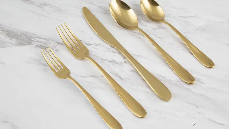 Golden flatware (knives, forks, spoons) sit together on a marble countertop.