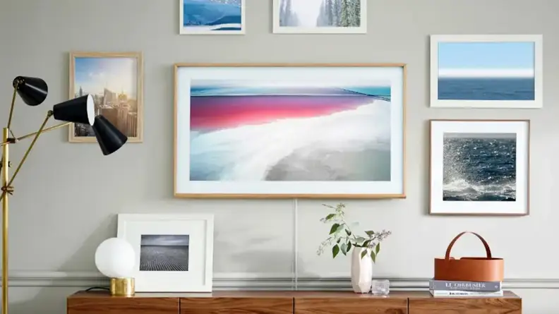 Assorted picture frames mounted on wall above wooden dresser and modern lamp.