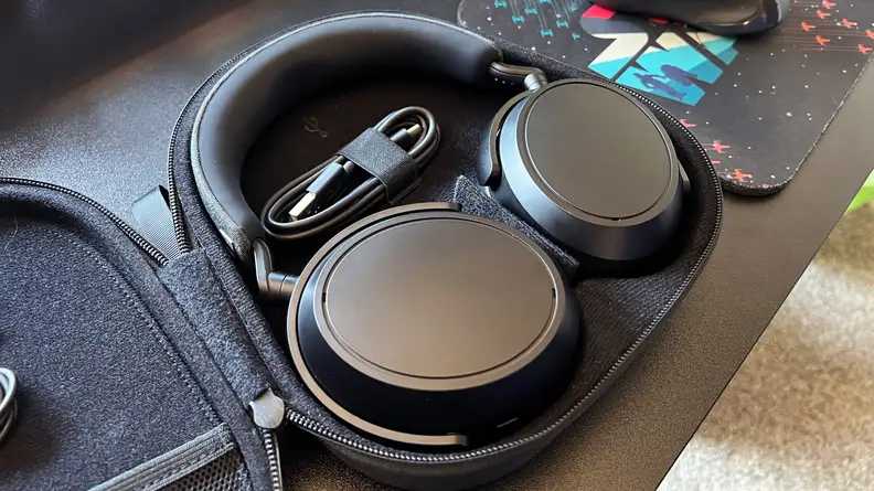 A black pair of headphones sit in their case on a black desk next to a star wars mousepad.