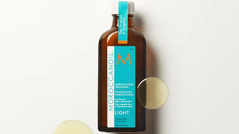 Bottle of moroccan oil with drops of oil on off-white background