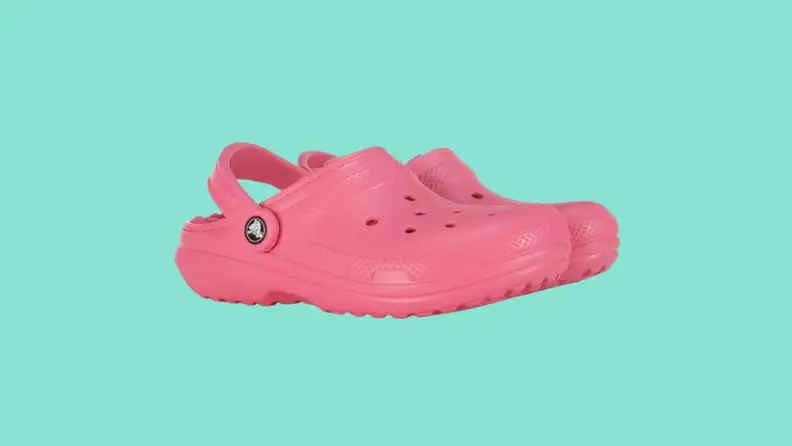 Side view of a pair of pink fuzz-lined Crocs on a dark teal background.