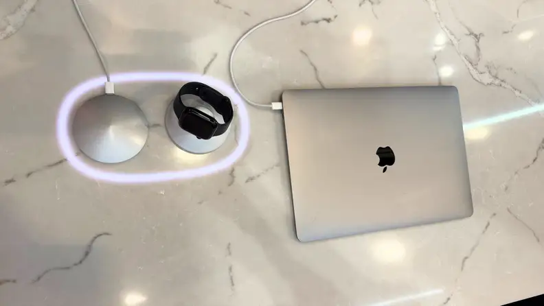 Smartphone and smartwatch wirelessly charging on an embedded FreePower surface integrated directly into a stone countertop beside a laptop.
