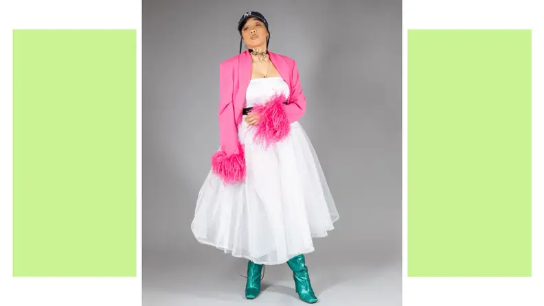 A person wearing a white tulle dress, a pink jacket with feathered sleeves, and green boots.