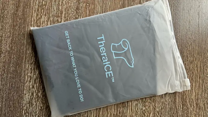 Black TheraIce RX Migraine Relief Cap inside of plastic bag on top of wooden surface.