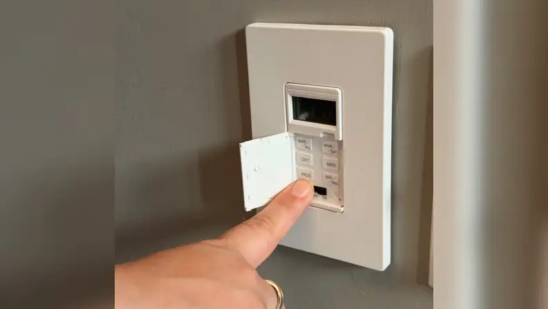 Small buttons on a Lider 7-Day Programmable Digital Timer Switch installed on a grey wall.