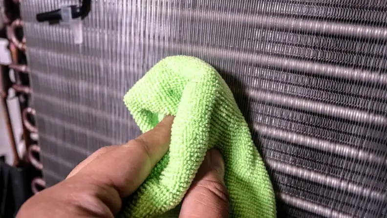 A close up of a person wiping the evaporator coils on their air conditioner unit.