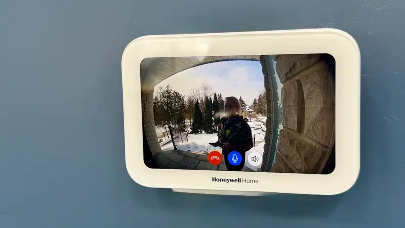 Screen of a Honeywell doorbell display mounted on a blue wall with a person shown at the door.