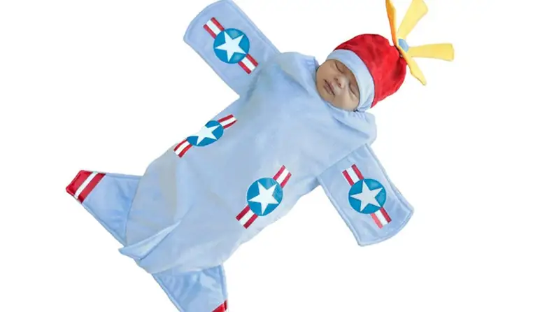 A baby lays down in a jet costume.