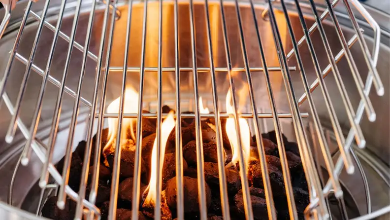 A close-up photo of hot charcoal briquettes covered with a metal grate.