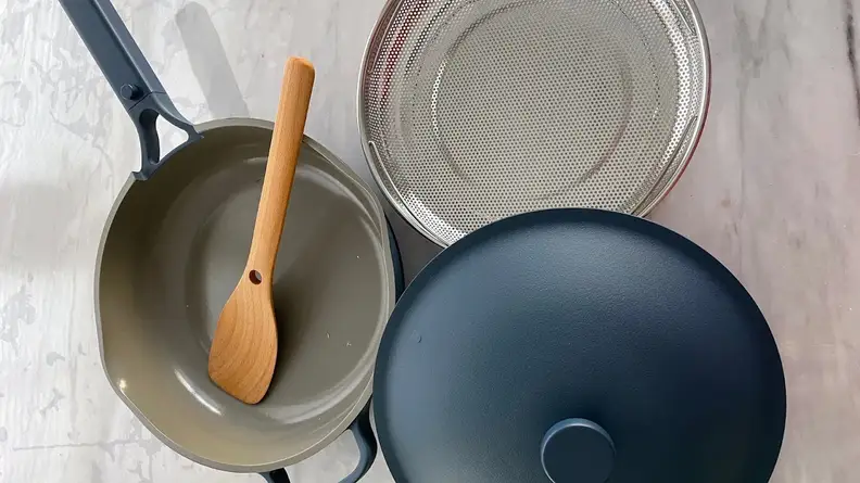 Always Pan 2.0 in Blue Salt color with lid, wooden spoon and steaming basket next to it.