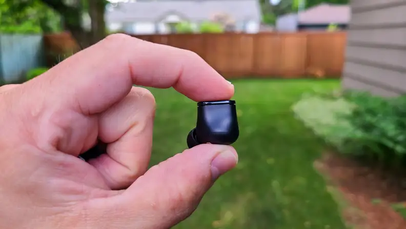 The black Beats Studio bud is held in fingers in front of a lush lawn and cedar fence.