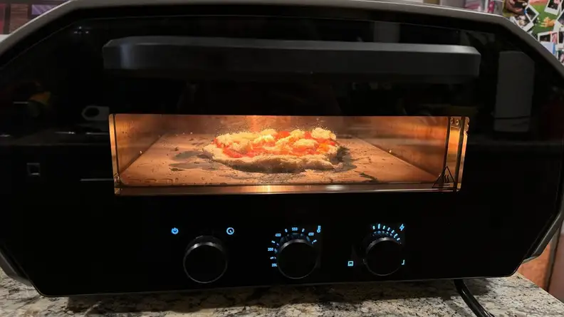 Raw pizza cooking inside of the Ooni Volt 12 pizza oven with door closed.