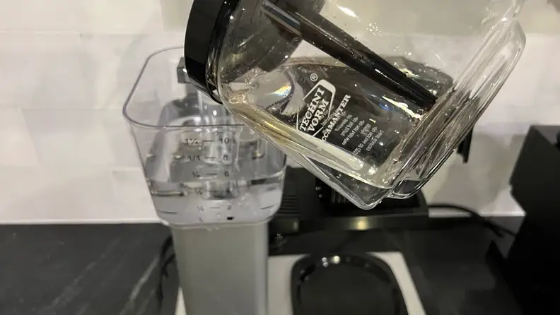 The Moccamaster glass pot being used to pour water into the reservoir.