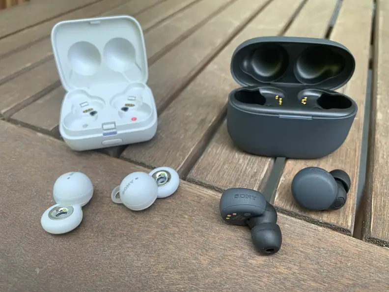 The black Sony LinkBuds S with their black charging case and the white Sony LinkBuds with their charging case sit on a wooden table.