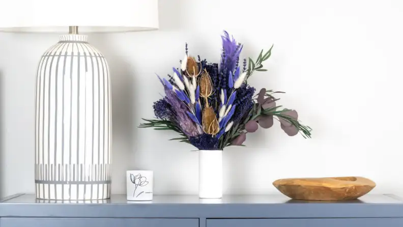 a white lamp sits next to a dried flower arrangement in a white vase on a blue table