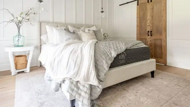 Mattress in modern bed frame with blankets and pillows in bedroom.
