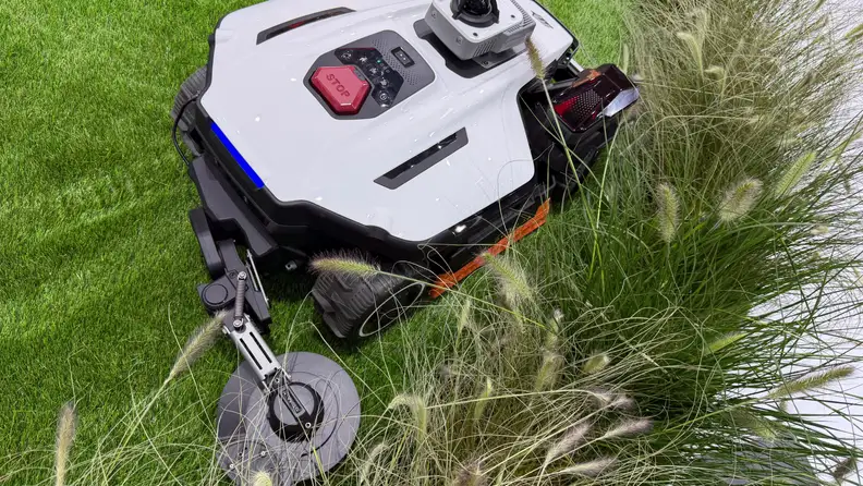 Close-up of the MAMMOTION LUBA 4 AWD with its edge-trimming attachment lowered, cutting through tall grass.