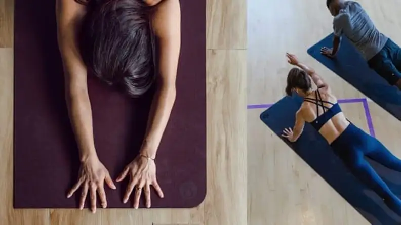 Left: Overhead view of a woman with arms stretched on a yoga mat. Right: A woman and man in athletic outfits stretching on a yoga mat.