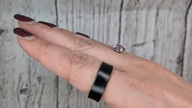 Samsung Galaxy Ring and a wedding ring on fingers of a hand on wooden background