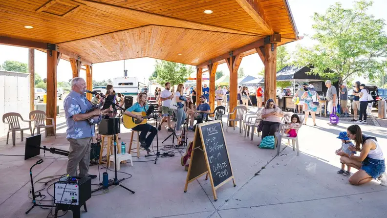 Musicians performing under a wooden pavilion at a farmers market