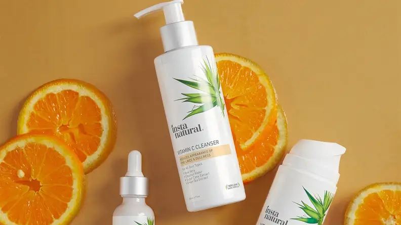 The InstaNatural Vitamin C Cleanser lays on a light brown background with orange slices and other InstaNatural products surrounding it.