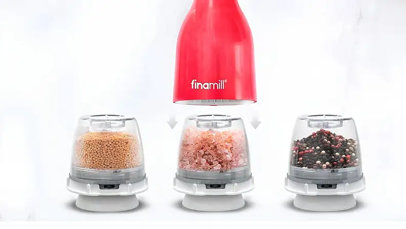 Finamill electric spice grinder shown with interchangeable pods containing mustard seeds, pink salt, and mixed peppercorns.