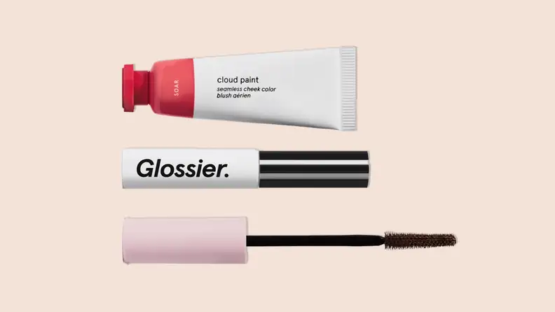 The Glossier "The Makeup Set" that includes Boy Brow, Cloud Paint and Lash Slick on a tan background.