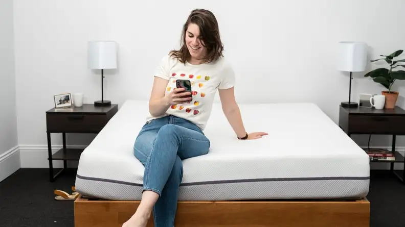 a person sits on the edge of a bed on their phone
