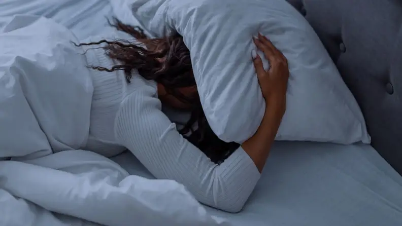 A person holds a pillow over their head in bed