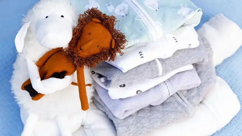 Stack of folded baby swaddles next to stuffed baby toys.