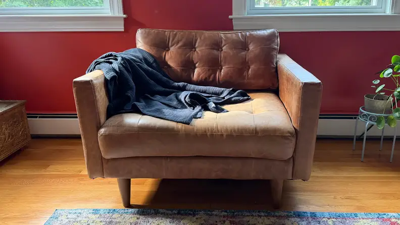 Navy blue Riley Home Four Layer Throw on a brown leather chair in front of a red wall on a wooden floor.