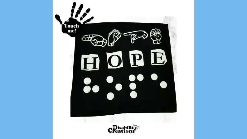 A Disability Creations T-shirt in braille on a blue background.