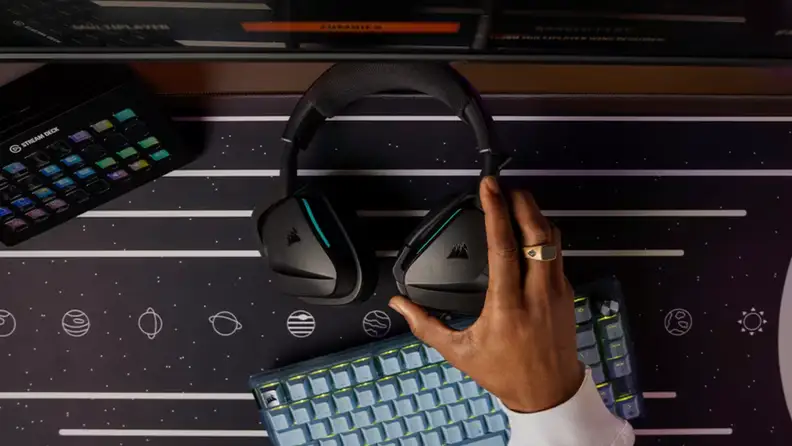 A hand reaches for a black Corsair headset resting on a space-themed gaming desk setup.