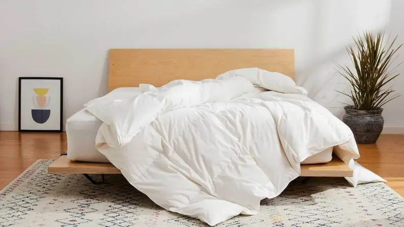 a brooklinen down comforter draped over the foot of a bed