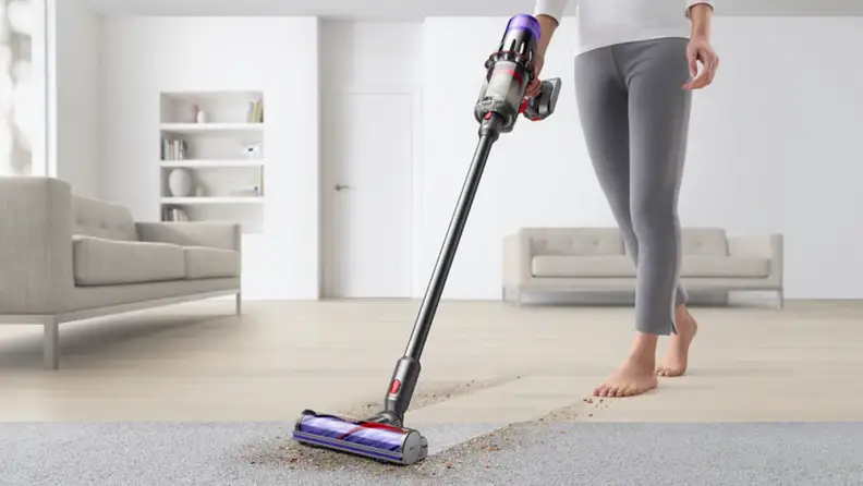 A person vacuums a carpet using a stick vacuum