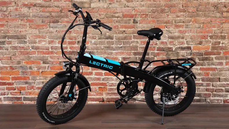 A Lectric XP 3.0 folding electric bike sits parked, next to a brick wall.