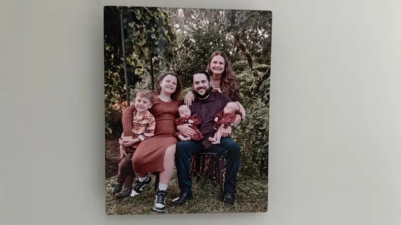 A metal photo print by Frameology showing a family of six hangs on a light gray wall
