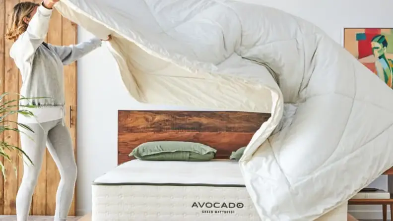A woman in the middle of making a bed, throwing a blanket on top of it.