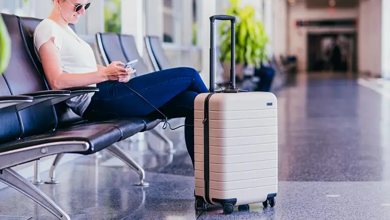 Person sitting in airport terminal next to suitcase