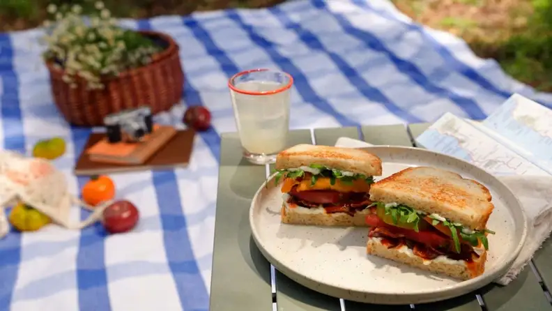A BLT sandwich on toasted bread with a glass of lemonade on a picnic blanket