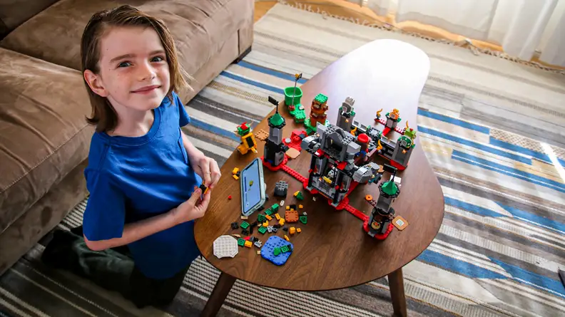 A child looks up proudly as he builds his Lego set.