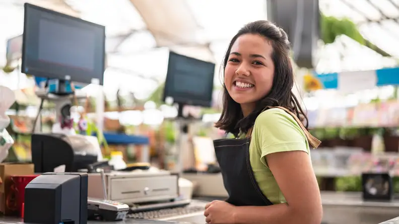 Young woman smiles while standing at a cash register in a grocery store